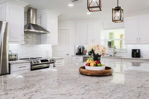 A modern kitchen with white cabinetry, stainless steel appliances, and a marble countertop. - Capecation! A Boater's Paradise, easy & quick out. (Cape Coral)