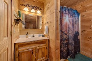 A wooden cabin bathroom with a wooden vanity, a mirror, and a shower curtain. - Sleeping Bear Hideaway (Sevierville)