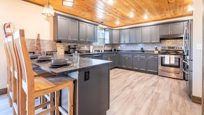 Une cuisine moderne avec un plafond en bois, des armoires grises, des appareils en acier inoxydable et un îlot central.