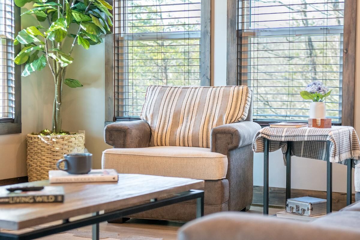 A cozy living room with a striped armchair, a coffee table, a potted plant, and a small table with a vase and books.