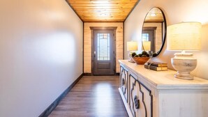 Un couloir avec un plafond en bois, une porte dotée d’une fenêtre, un miroir et une lampe posée sur une console.