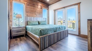 Un dormitorio con cabecera de madera, una cama con cubrecama verde, dos ventanas y una mesita de noche.