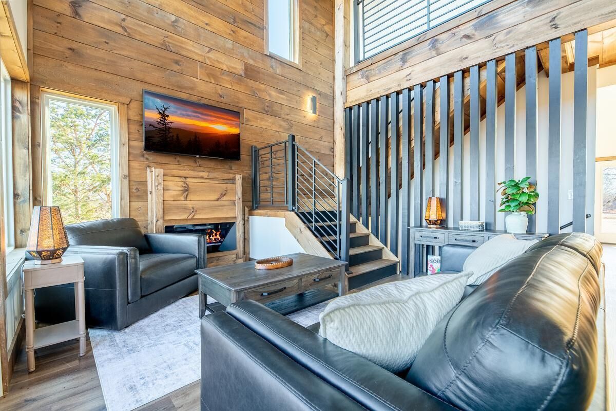 Un salon moderne avec une cheminée, des canapés en cuir, un téléviseur et un escalier.