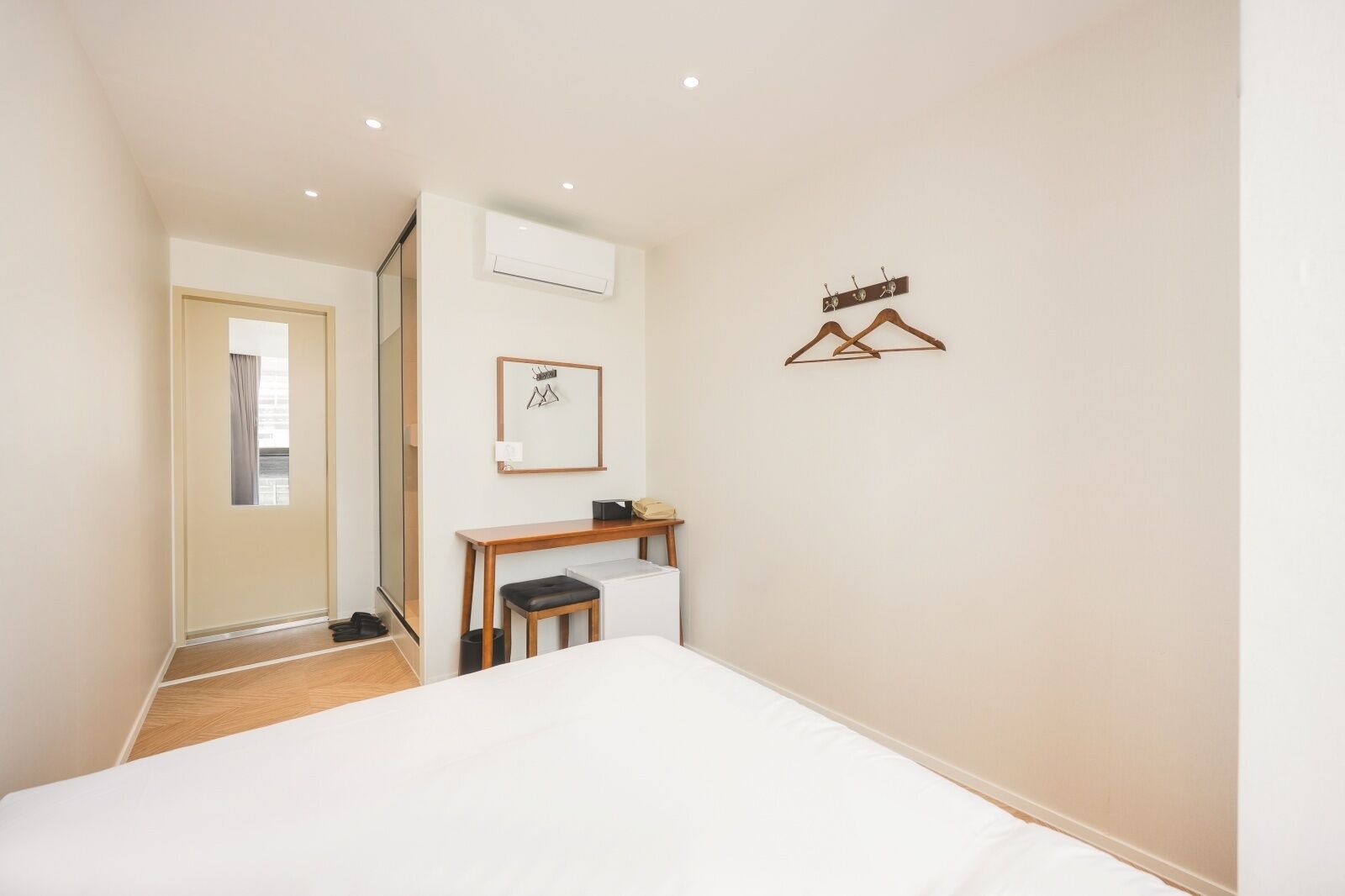 Un dormitorio con cama, escritorio, silla, equipo de aire acondicionado y perchero.