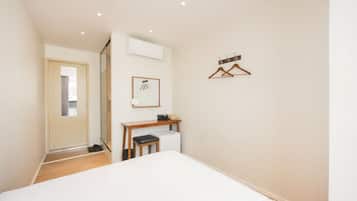 Un dormitorio con cama, escritorio, silla, equipo de aire acondicionado y perchero.