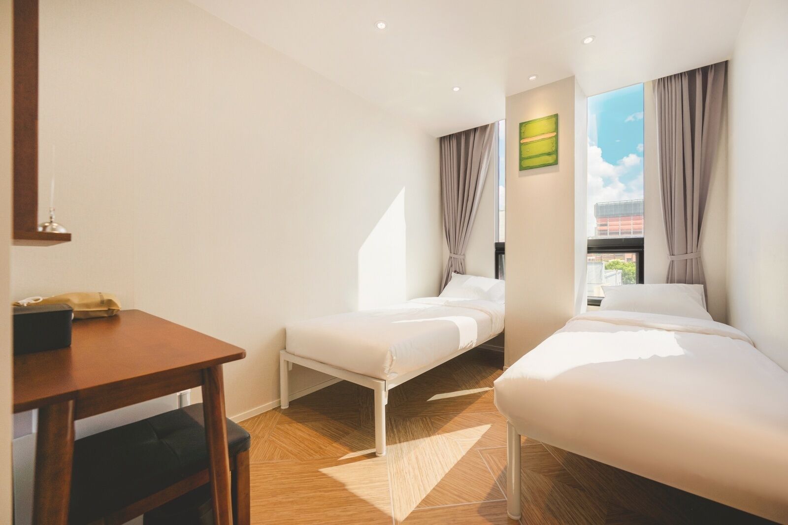 A hotel room with two beds, a wooden table, a small desk, and a window with curtains.