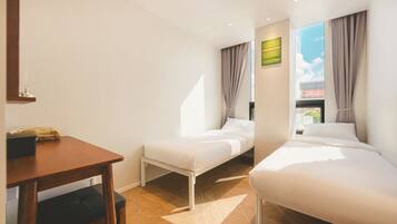 A hotel room with two beds, a wooden table, a small desk, and a window with curtains.