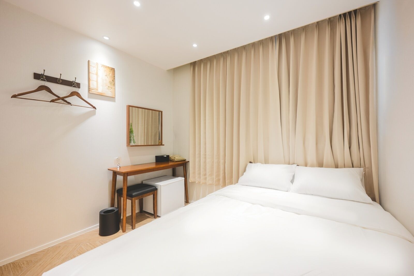 Habitación de hotel con cama, escritorio, silla, perchero y espejo.