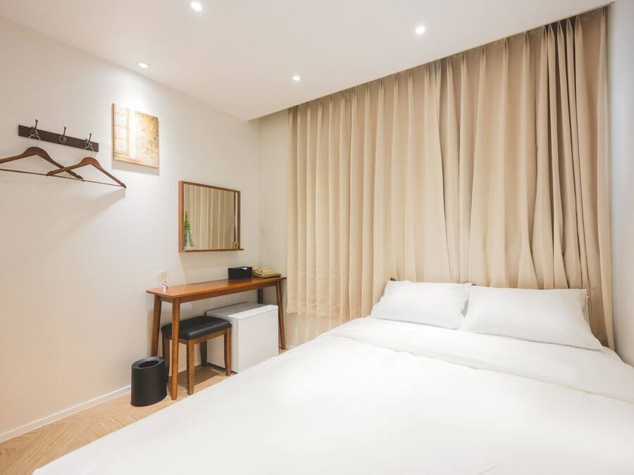 Habitación de hotel con cama, escritorio, silla, perchero y espejo.