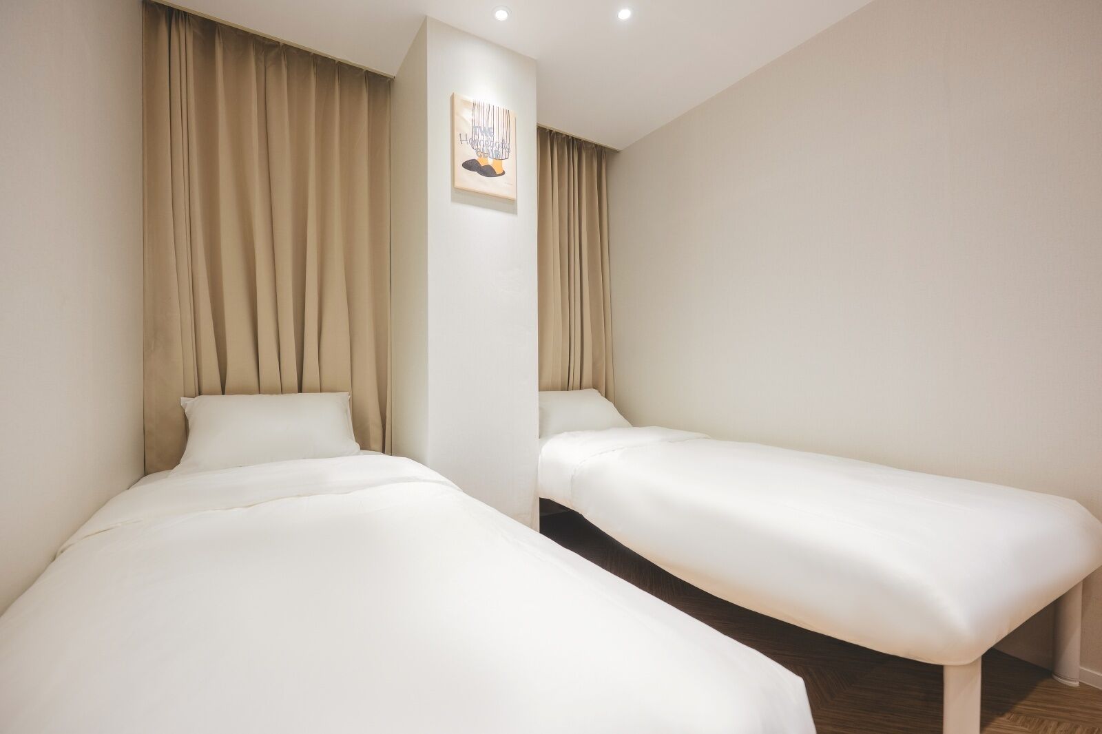 Two single beds in a room with beige curtains and a framed picture on the wall.