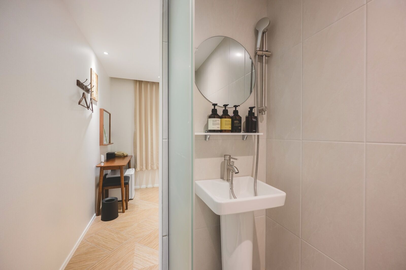Un baño moderno con un lavabo blanco, un cabezal de ducha de mano y un espejo. Hay un estante con artículos de aseo y una mesita con una silla.