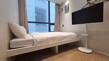 A room with a bed, a TV mounted on the wall, and a window with curtains.