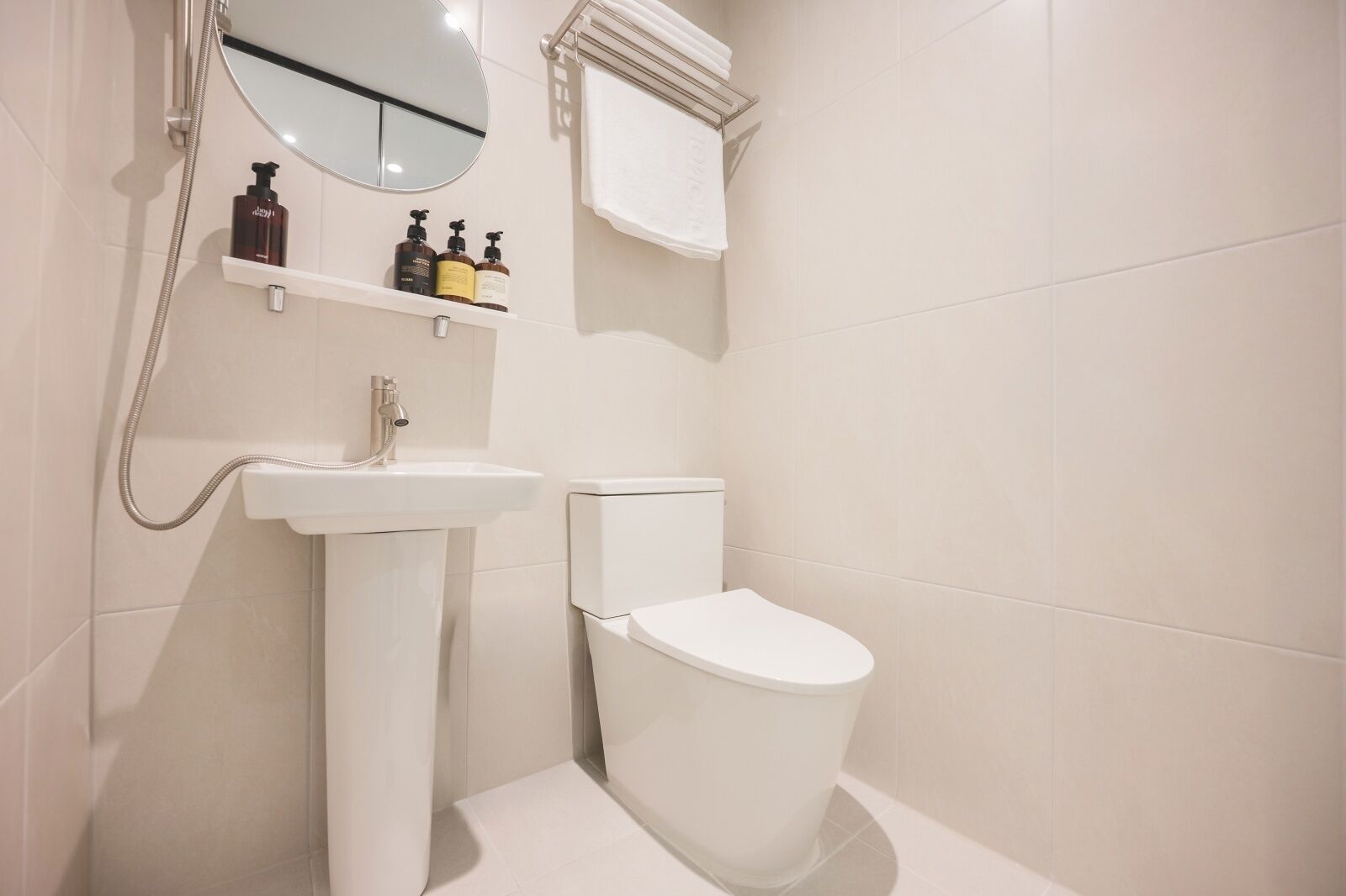 A bathroom with a white sink, a toilet, and a mirror above the sink. There are two bottles on the shelf above the sink.