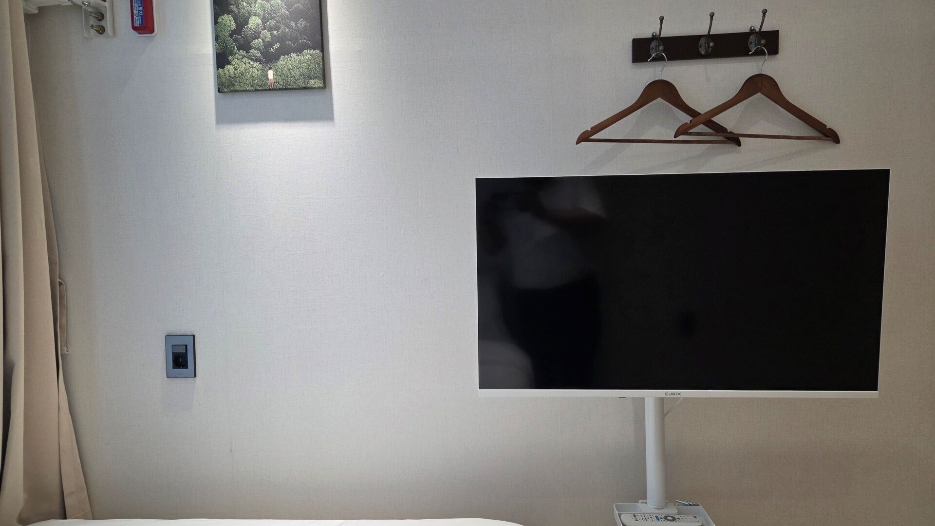 A room with a large flat-screen TV mounted on the wall, a power outlet, and a coat rack with hangers.