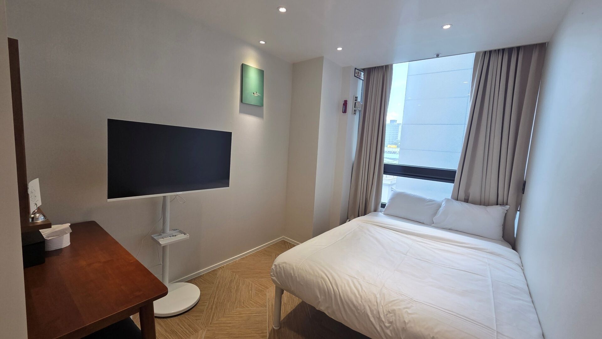 Quarto de hotel com cama, televisão de tela plana, uma mesinha e uma janela com cortinas.