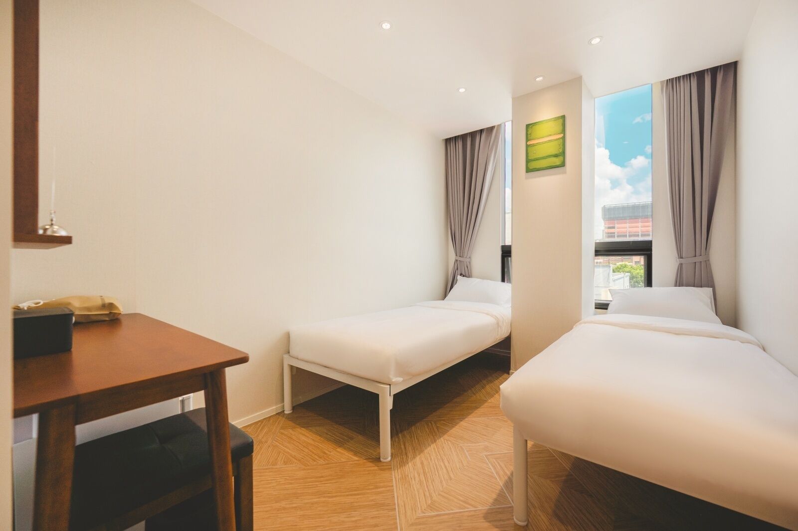 Een hotelkamer met twee eenpersoonsbedden, een houten bureau, een telefoon en een raam met gordijnen.