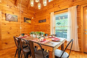 A wooden cabin interior with a dining table set for four, surrounded by chairs, and a sign on the wall. - Owl Be Back (Pigeon Forge)