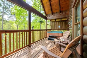 A wooden deck with a hot tub, chairs, and a view of the forest. - Owl Be Back (Pigeon Forge)