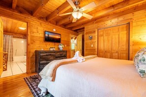 A wooden cabin interior with a bed, a ceiling fan, a mounted TV, and a wooden door. - Owl Be Back (Pigeon Forge)