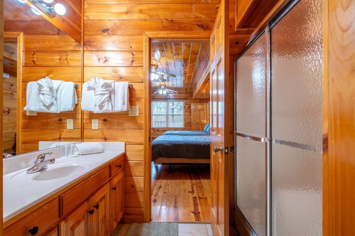 A wooden cabin-style bathroom with a double sink, a mirror, and a shower area.