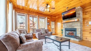 Ein gemütliches Blockhaus-Interieur mit Kamin, Ledersofas, einem Couchtisch und einem Fernseher.