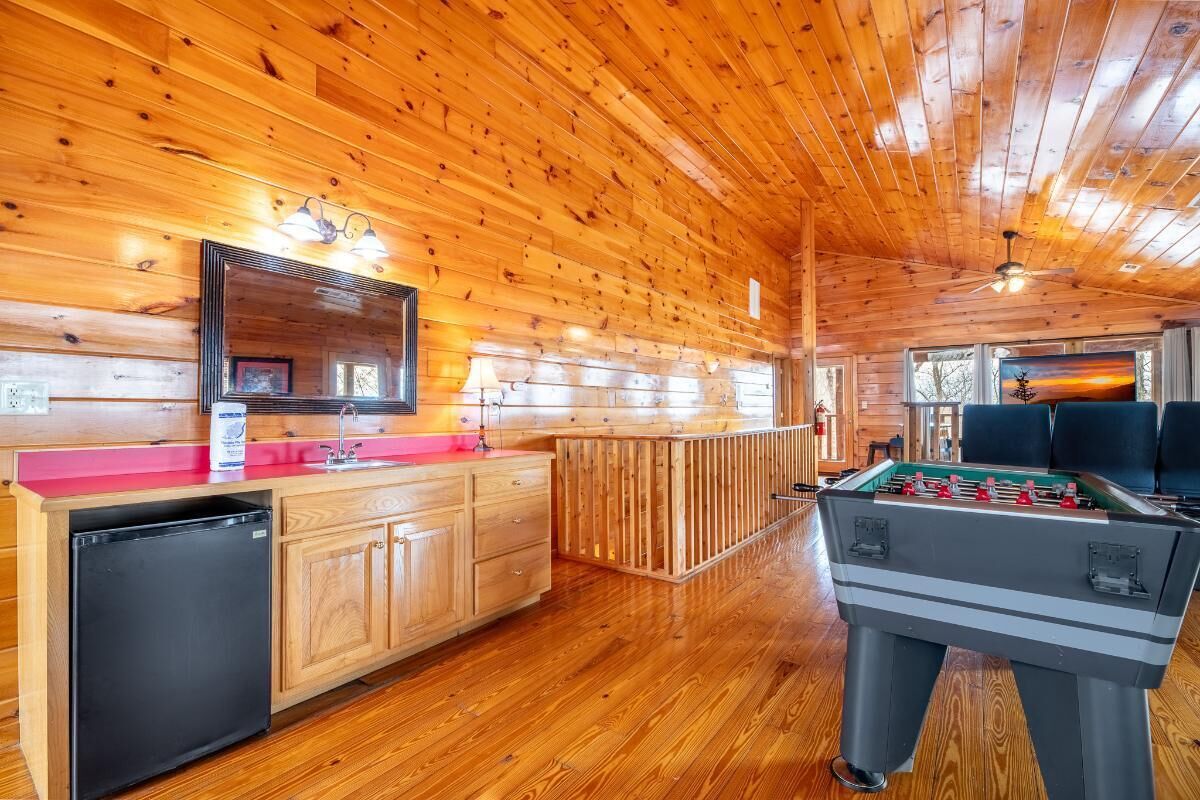 A wooden interior with a foosball table, a refrigerator, and a large mirror.