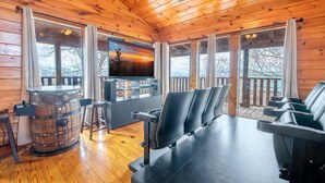 Ein Ferienhaus-Interieur mit Holzwänden, einem großen Fernsehbildschirm, einer Bar und Sitzgelegenheiten.