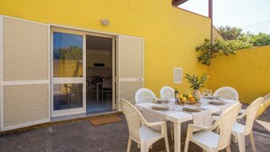 A yellow building with a sliding glass door entrance, a table set with white chairs, and a small garden area with a plant. - SpiaggiaSogno da Giò (San Teodoro)