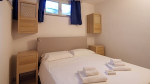 A neatly made bed with white linens, two wooden nightstands, and a window with blue curtains. - SpiaggiaSogno da Giò (San Teodoro)