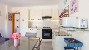 A compact kitchen with white cabinets, a gas stove, a microwave, and a small oven. There is a dining table with chairs and a vase of flowers. - SpiaggiaSogno da Giò (San Teodoro)