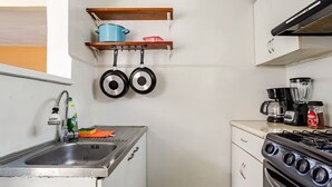 Eine kleine Küche mit Spüle, Herd und hängenden Töpfen.