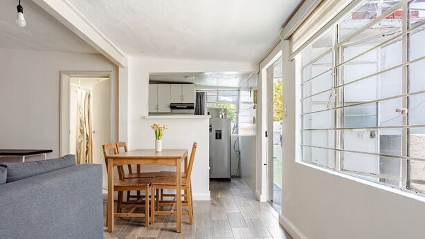 Eine Küche mit Esstisch, Stühlen, einem Kühlschrank und einem Fenster mit Jalousien.