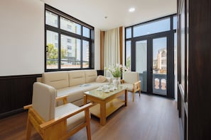 A modern living room with a sofa, two armchairs, a glass coffee table, and a view of the city through large windows. - Kinh Do Hotel (Hue)