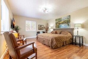Ein Schlafzimmer mit einem großen Bett, einem Sessel, einem Fernseher und einem Gemälde an der Wand.