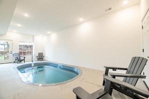 An indoor swimming pool with a chair and a table, a door, and a view of the outside. - The Playhouse (Sevierville)