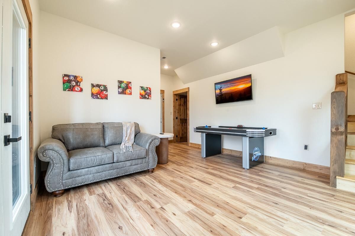 A living room with a gray sofa, wooden flooring, a foosball table, and wall art.