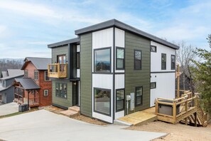 A modern multi-story house with a balcony, a wooden deck, and a small porch. - The Playhouse (Sevierville)