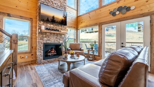 A cozy living room with a stone fireplace, leather sofa, and a TV mounted on the wall. - Take It Easy (Sevierville)