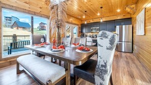 A modern interior with a wooden ceiling, a dining area with a bench, a kitchen with stainless steel appliances, and a view of buildings outside. - Take It Easy (Sevierville)