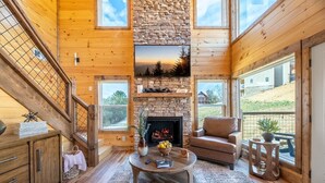 A cozy cabin interior with a stone fireplace, wooden walls, a comfortable seating area, and a balcony with a view. - Take It Easy (Sevierville)