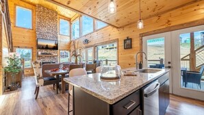 A spacious kitchen with a large island, wooden ceiling, and a stone fireplace. - Take It Easy (Sevierville)