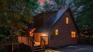A wooden cabin with a staircase leading to a deck, surrounded by trees. - Bear Run Getaway (Gatlinburg)