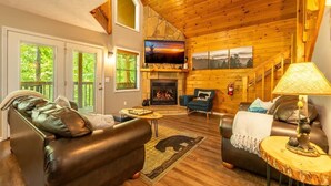 A cozy log cabin interior with a fireplace, leather sofas, and a television. - Bear Run Getaway (Gatlinburg)