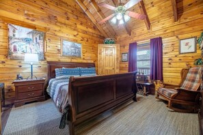 A wooden cabin bedroom with a bed, dresser, chair, and ceiling fan. - Starwood (Sevierville)