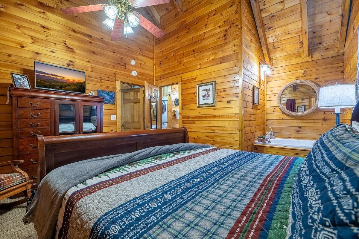 A wooden cabin bedroom with a bed, dresser, mirror, and ceiling fan.
