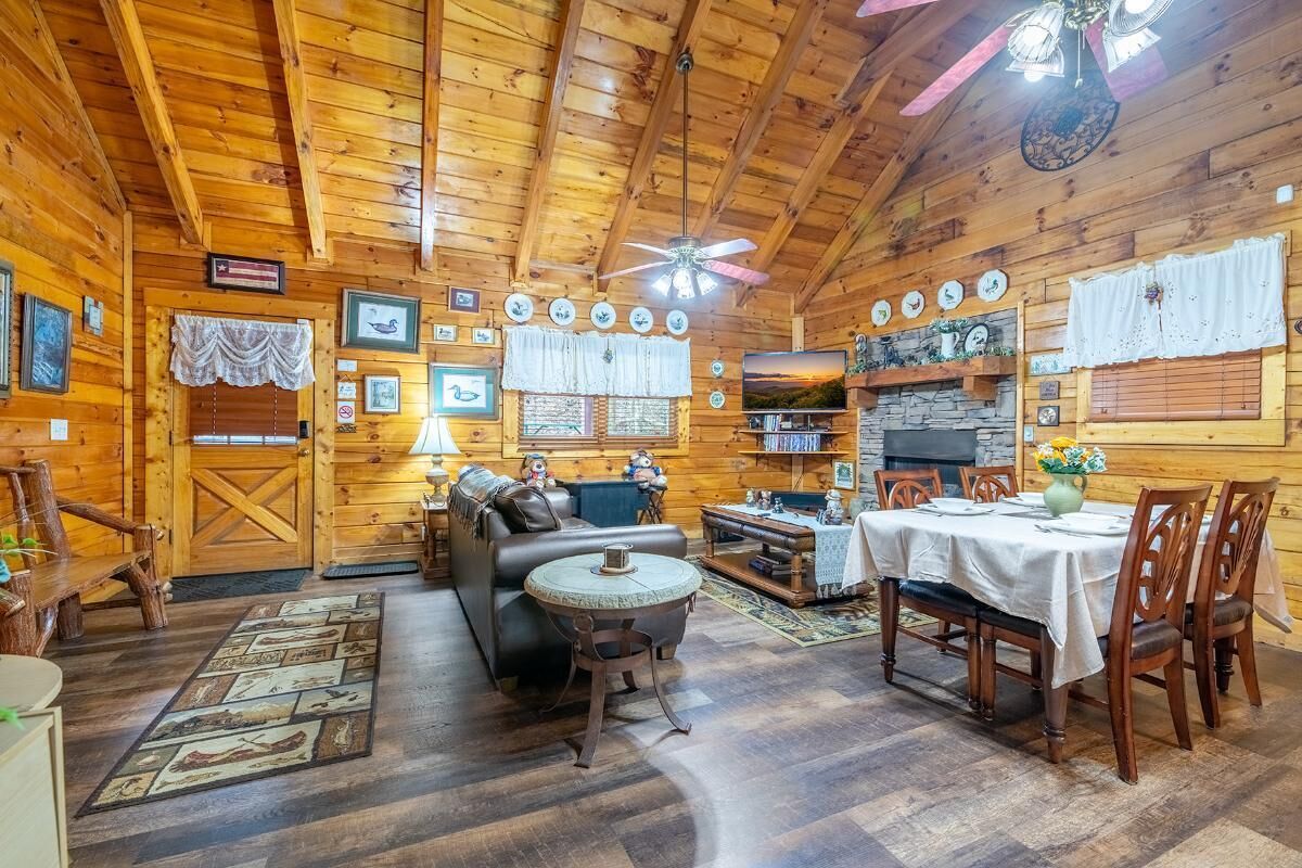 A log cabin interior with a fireplace, wooden walls, a dining table, and a sofa.