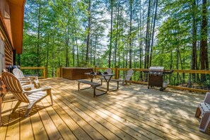 A wooden deck with outdoor furniture, a grill, and a view of a forest. - Call of the Wild (Sevierville)