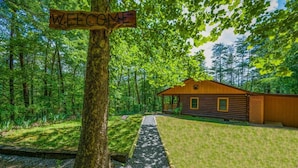 Eine Holzhütte mit einem 'WELCOME'-Schild, umgeben von einem Wald.