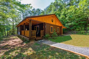 A log cabin with a porch, surrounded by a forest. - Call of the Wild (Sevierville)
