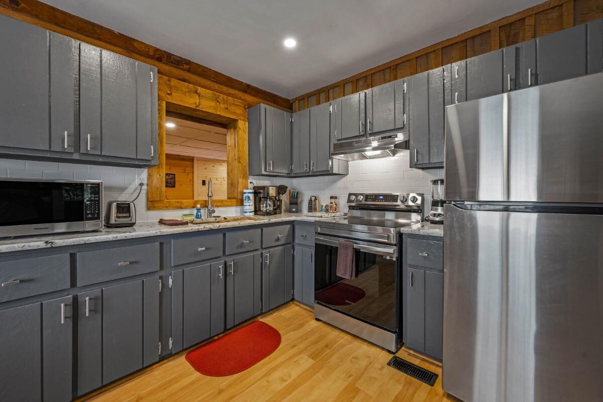 A modern kitchen with grey cabinets, stainless steel appliances, and wooden accents.